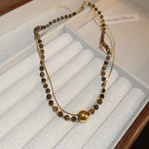 Détail d'un collier double épaisseur plaqué or 18 carats avec perles œil de tigre et boule d'or