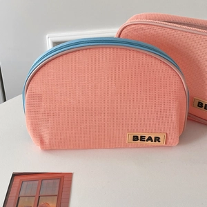 Detail of a pink mesh semi-circle makeup bag with blue zipper and BEAR logo tag