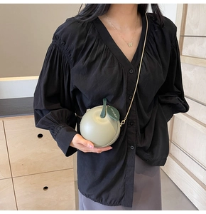 Detail of light green apple-shaped bag featuring leather leaf and gold chain strap