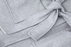 Détail d'un manteau en laine gris montrant la texture douce, les coutures et la ceinture