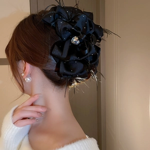 Close-up of black satin flower hair claw clip with feathers and heart-shaped gemstone