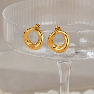 Detail of gold-plated irregular circular earrings hanging on textured glass