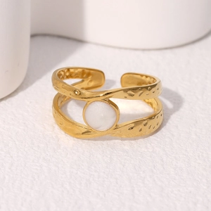 Golden geometric open ring with wavy texture and white gemstone on a white surface