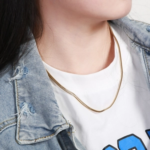 Close-up of a delicate gold snake chain necklace worn with a denim jacket