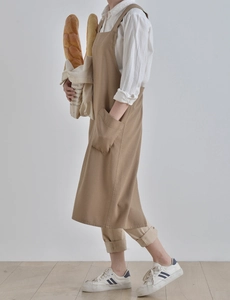 Detail of khaki cotton-linen apron featuring a large front pocket and wide shoulder straps
