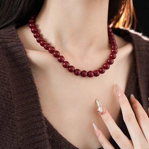 Close-up of deep red beaded titanium steel necklace on a dark knitted sweater background