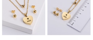 Macro detail of gold plated heart pendant with mãe engraving and round stud earrings set