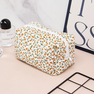Close-up of quilted floral cosmetic bag with orange flower pattern on marble background