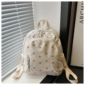 Detailed view of the small floral pattern and zippers on the cream-colored nylon backpack