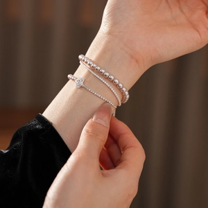 Détail de bracelets superposés avec fleur en zircon et perles sur chaîne argentée ajustable