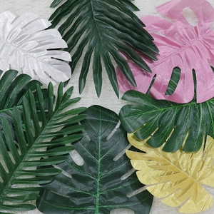 Flat lay of colorful artificial monstera leaves in gold and pink on white fur backdrop
