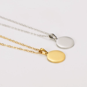 Polished gold and silver stainless steel round disc pendant necklaces on grey surface
