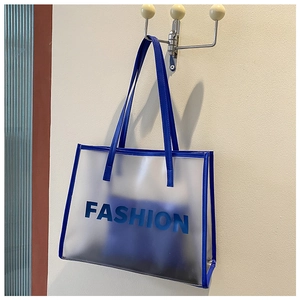 Close-up of blue transparent PVC tote bag with FASHION lettering and leather trim detail