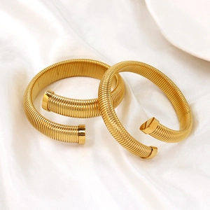 Detailed macro of two gold cuff bracelets with spiral texture on white silk background