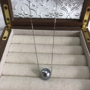Detailed view of gray-purple pearl pendant on silver chain inside a wooden jewelry box