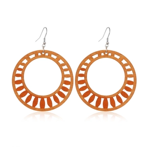 Detail view of round hollow wooden earrings with geometric sunburst patterns in brown