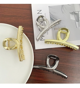 Flat lay of four large metal hair claws in gold, silver, and gunmetal on a wooden table