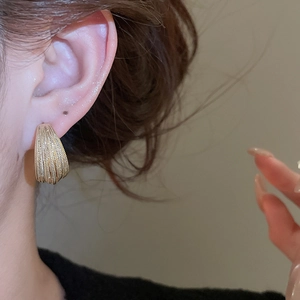 Close-up of gold-plated multi-layer C-shaped stud earrings with striped metal texture