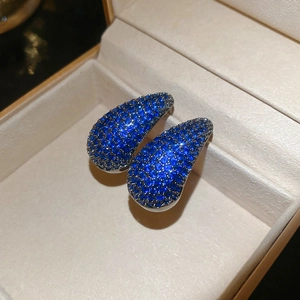 Detail shot of silver drop earrings with blue zircon pavé stones on beige velvet cushion