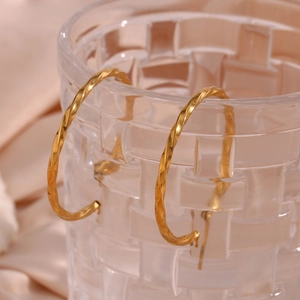 Macro detail of gold-plated twisted hoop earrings on a textured glass rim