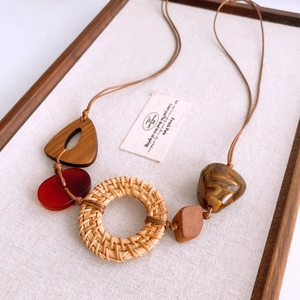 Detail of bohemian rattan circle pendant with wood and resin charms on a brown rope chain