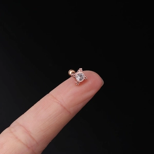 Macro shot of rose gold stud earring with round zircon held on fingertip for scale