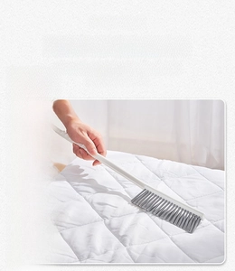 Macro detail of long handle brush with grey bristles cleaning a white quilted mattress