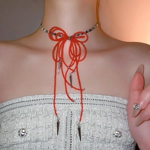 Detail of red beaded bow necklace with silver metal spikes and tassel on a female model
