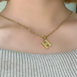 Dettaglio della collana con ciondolo a lettera H dorata e catena Figaro su modella