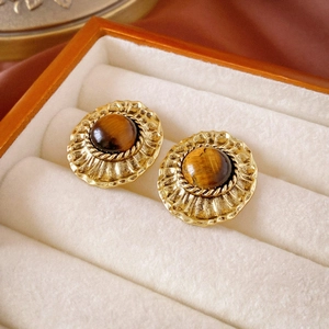 Macro shot of tiger eye stone earrings with gold textured borders in a wooden jewelry box