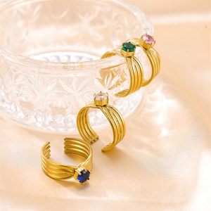 Detalle de tres anillos dorados con capas y circonitas en colores azul, transparente y verde