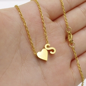 Detail shot of golden heart pendant and letter S charm on a sleek stainless steel necklace