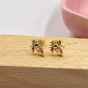 Macro shot of gold beetle earrings with pink drop-shaped stones on wood surface