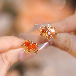 Macro shot of gold maple leaf earrings with gradient orange red crystals on fingertips