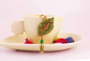 Detail of green rhinestone encrusted lip keychain with small lipstick charm on a gold base