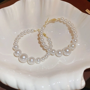 Macro detail of faux pearl hoop earrings with gradient sizing in a white shell tray