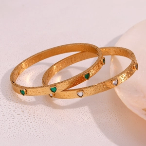 Macro detail of 18K gold-plated bracelets with heart-shaped gems and water droplets