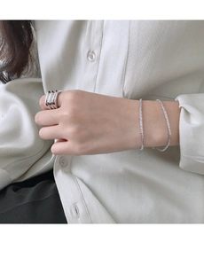 Macro shot of a layered silver ring and thin beaded bracelet on a minimalist shirt