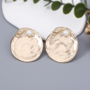 Detail of golden hammered metal round earrings featuring a single white pearl accent