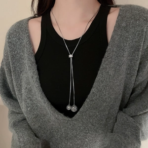 Close-up of a long adjustable silver necklace with a hollow sphere pendant on a model