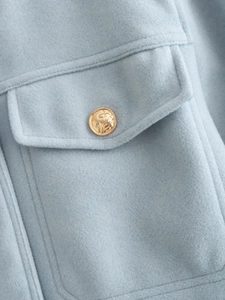 Detail of light blue tweed jacket showing textured fabric with gold embossed button