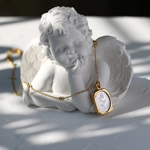 Detailed view of vintage gold rose pendant necklace on elegant white angel statue