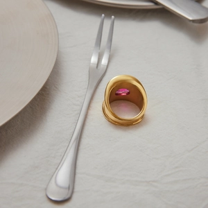 Close-up of a gold stainless steel ring with a rectangular pink zircon on white fabric