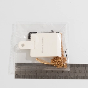 Flat lay of gold tube necklace on white background with metal ruler showing 5cm pendant size