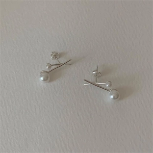 Detail of silver crossover pearl earrings featuring a minimalist geometric design