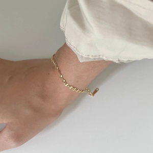 Macro shot of minimalist gold twisted chain link bracelet with polished metal tag charm