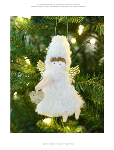 Close-up of white plush Christmas angel doll with golden wings hanging on a warm lit tree