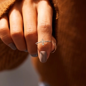 Close-up of a tiny silver cross ring with pavé zircons worn on index finger