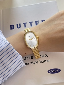 Elegant gold oval watch with segmented steel strap shown on a wrist over a book