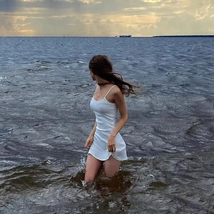 Detail of white slim-fit strap dress worn by a model standing in the sea at beach